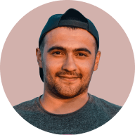 Smiling man wearing a backward black cap and gray shirt with a beige background.